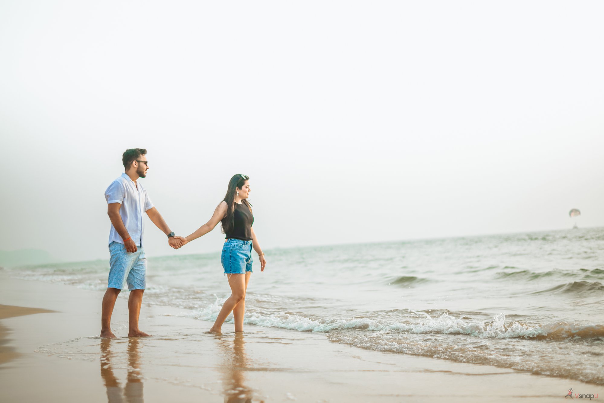 Love and laughter—pre-wedding couple walking along the shoreline, eyes full of happiness.